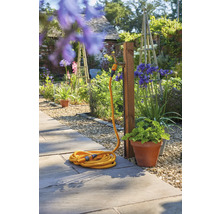 Gartenszene mit aufgerollten Gartenschlauch und Wasserhahn an einem Holzpfosten