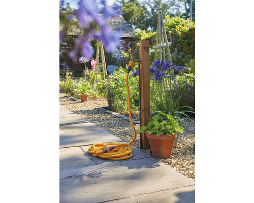 Gartenszene mit aufgerollten Gartenschlauch und Wasserhahn an einem Holzpfosten