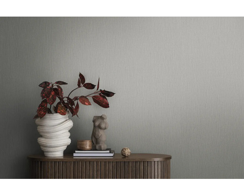 Detailaufnahme einer grauen Strukturtapete mit Pflanze und Dekorationsgegenständen auf einem Holztisch