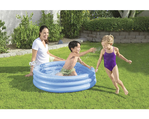 Aufblasbares Planschbecken mit spielenden Kindern und einer Frau im Garten.