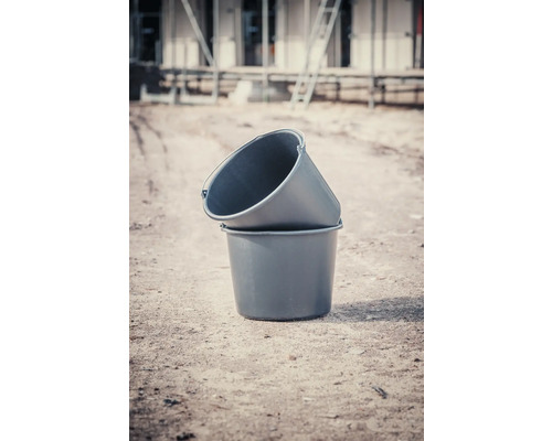 Zwei Mörtelkübel aus Kunststoff stehen übereinander auf einer Baustelle.