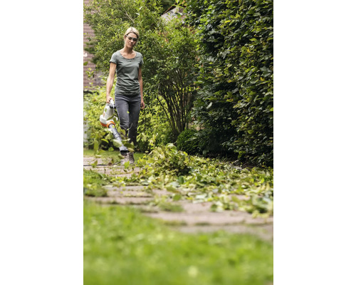 Frau benutzt einen Laubbläser im Garten, um gefallenes Laub zu entfernen.