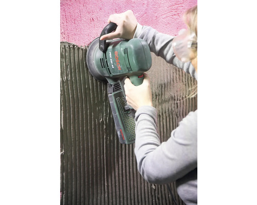 Eine Person verwendet einen Bosch Exzenterschleifer, um eine Wand zu schleifen.