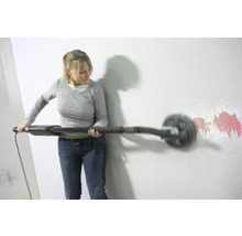 Eine Frau schleift eine Wand mit einem Langhalsschleifer, um Farbreste zu entfernen.