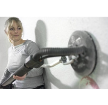 Eine Frau verwendet einen Trockenbauschleifer an einer Wand.