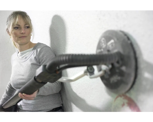 Eine Frau verwendet einen Trockenbauschleifer an einer Wand.