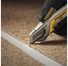 Eine Person schneidet mit einem Teppichmesser Teppich zu. Das Teppichmesser ist von Stanley.