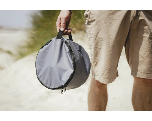 Graue, runde Tragetasche mit Reißverschluss in der Hand einer Person