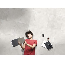 Eine Frau liegt auf dem Boden mit Fliesen, umgeben von einem Tablet, einem Smartphone, Notizbüchern und einer Tasse.
