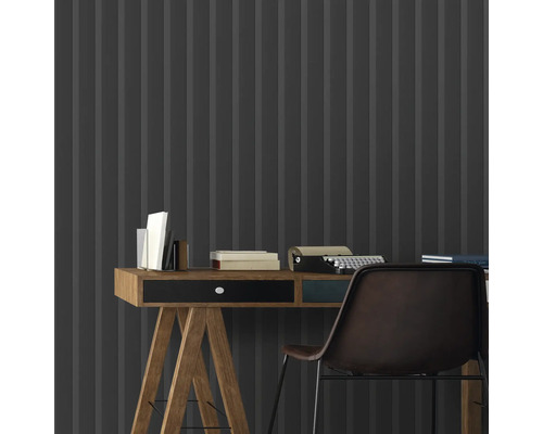 Nahaufnahme eines Schreibtisches mit Büchern und einer Schreibmaschine vor einer grauen Wandtapete mit Streifenmuster.