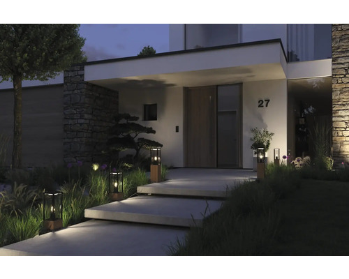 Eingangsbereich eines Hauses mit Steinmauer, Treppenstufen, Pflanzen und Außenleuchten