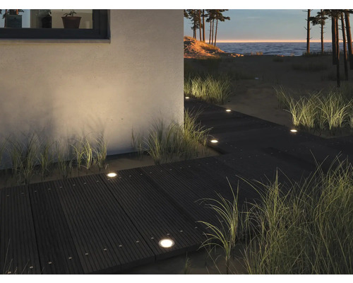 Szene mit einem Holzsteg, der mit eingelassenen Leuchten beleuchtet wird und zu einem Strand führt.