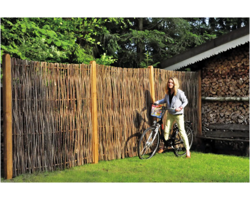 Gartenszene mit einem Zaun aus Naturmaterialien und einer Frau mit Fahrrad