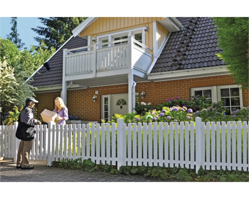 Person übergibt ein Paket vor einem Haus mit weißem Zaun