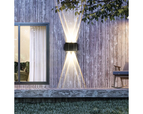 Beleuchtete Außenwandleuchte an einer Holzwand neben einem Fenster und einem Schaukelstuhl.