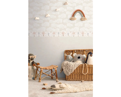 Dekoriertes Kinderzimmer mit Wolken Tapete, Regenbogen Wanddeko, Rattanhocker und Spielzeug in einem Korb.