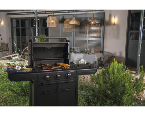 Schwarzer Gasgrill mit Speisen im Garten mit Beleuchtung