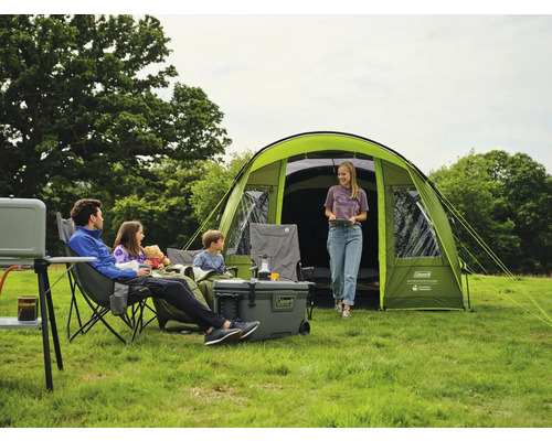Eine Familie entspannt sich beim Camping vor einem Zelt mit Kühler, Stühlen und Tisch.