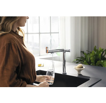 Frau füllt Wasser in eine Glasflasche unter einem Wasserhahn in einer modernen Küche.