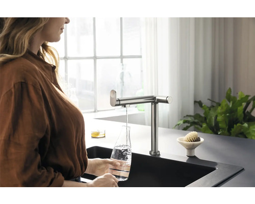 Frau füllt Wasser in eine Flasche unter einem Küchenarmatur
