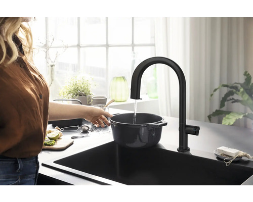 Eine Person befüllt einen Kochtopf mit Wasser aus einer schwarzen Küchenarmatur in einer modernen Küche.