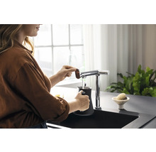 Frau bereitet mit einem Wasserhahn und einem schwarzen Behälter in der Küchenspüle ein Getränk zu.