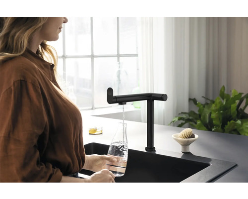 Frau befüllt Wasserflasche am schwarzen Küchenarmatur