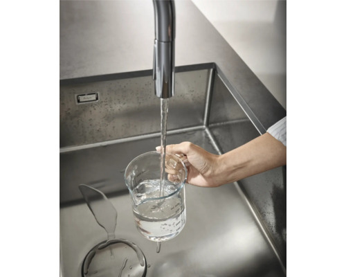 Edelstahlspüle mit Wasserhahn und Messbecher, der mit Wasser befüllt wird.