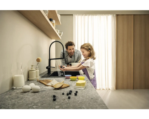 Szene in einer Küche mit einem Vater und seiner Tochter, die Blaubeeren unter einem Wasserhahn waschen, während sie zusammen kochen