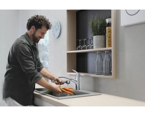 Mann wäscht Karotten in einer modernen Küche mit Spültischarmatur