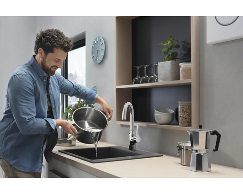 Ein Mann gießt Wasser aus einem Kochtopf in ein Spülbecken in einer modernen Küche.