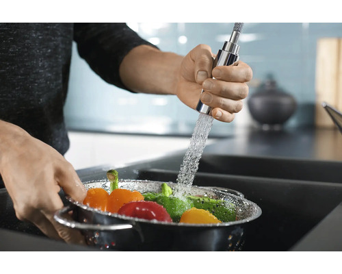 Gemüse wird in einem Küchensieb unter einem Wasserhahn gewaschen.