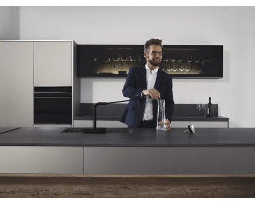 Moderne Küche mit elegantem Design und Mann, der Wasser in eine Karaffe füllt