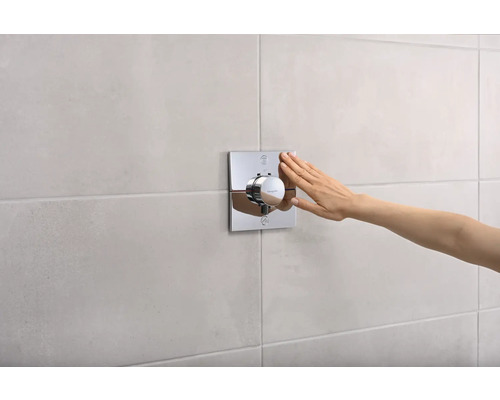 Aufputz-Thermostat mit Hand auf Fliesenwand montiert