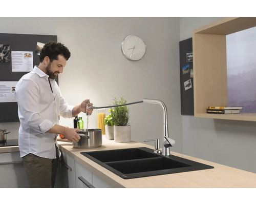 Mann füllt Wasser in einem modernen Küchenspüle mit ausziehbarer Armatur.