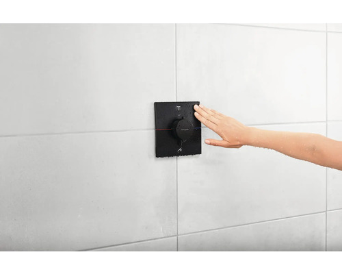 Eine Hand reguliert einen Duschthermostat der Marke Hansgrohe an einer gefliesten Wand