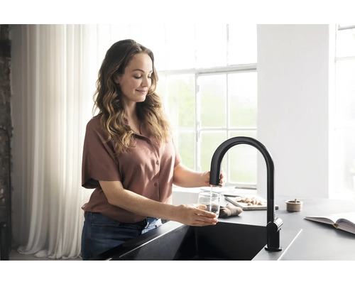 Frau füllt Wasser in ein Glas an einem schwarzen Wasserhahn in der Küche