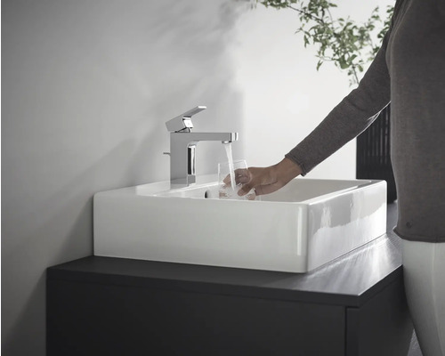 Person befüllt Glas unter einem Wasserhahn in einem Waschbecken