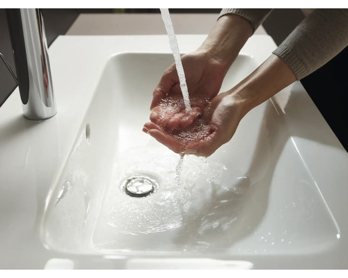 Hände werden in einem weißen Waschbecken unter einem Wasserhahn gewaschen