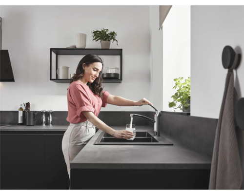 Frau füllt Glas Wasser am Küchenwaschtisch mit Armatur.