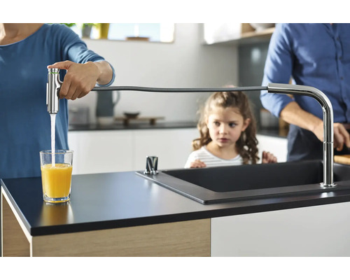 Eine Familie in einer hellen Küche, wobei die Mutter ein Glas mit einem Wasserhahn mit Schlauch füllt