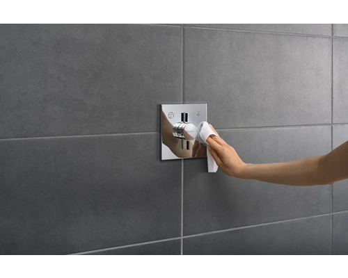 Hand reinigt eine Duscharmatur mit einem Tuch