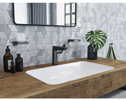 Badezimmerwaschtisch mit Aufsatzwaschbecken, Armatur, Spiegel und Accessoires vor einer Wand mit geometrischen Fliesen