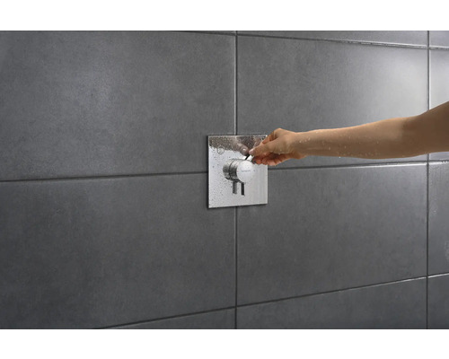 Nahaufnahme einer Hand, die einen Duschmischer an einer gefliesten Wand bedient