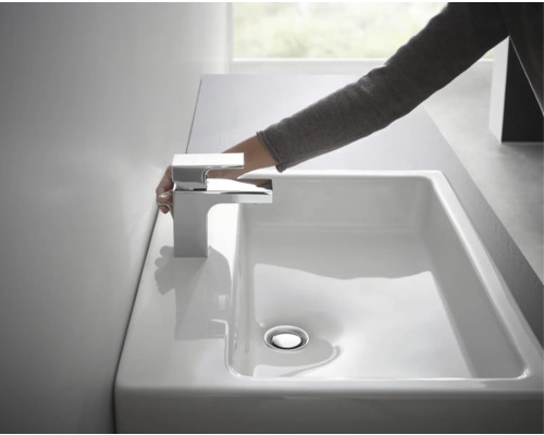 Hand am Chrom Wasserhahn über einem weißen Waschbecken