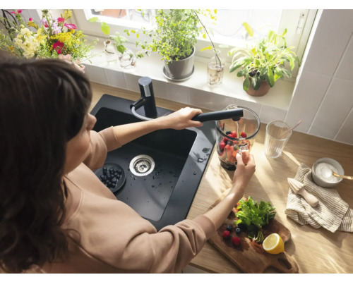 Frau befüllt einen Mixer mit Wasser an einem Spültisch mit Armatur in einer Küche.