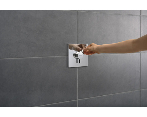 Hand betätigt Duscharmatur mit quadratischer Blende an grauer Wand