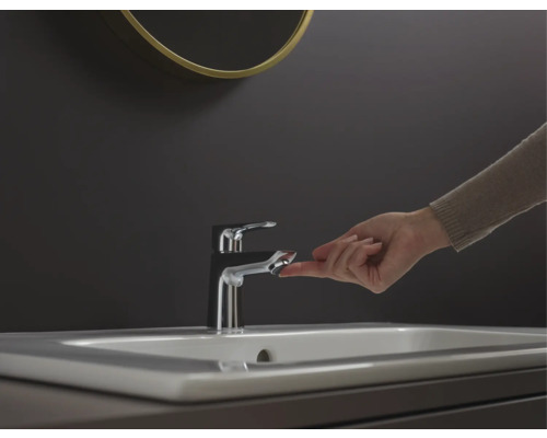 Waschbeckenarmatur mit Finger auf dem Bedienknopf in einem Badezimmer.