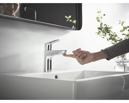 Waschtischarmatur aus Metall auf einem Waschbecken mit einer Hand, die den Wasserhahn berührt