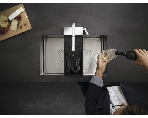 Edelstahlspüle mit Zubehör und einer Person, die ein Glas Wein einschenkt.